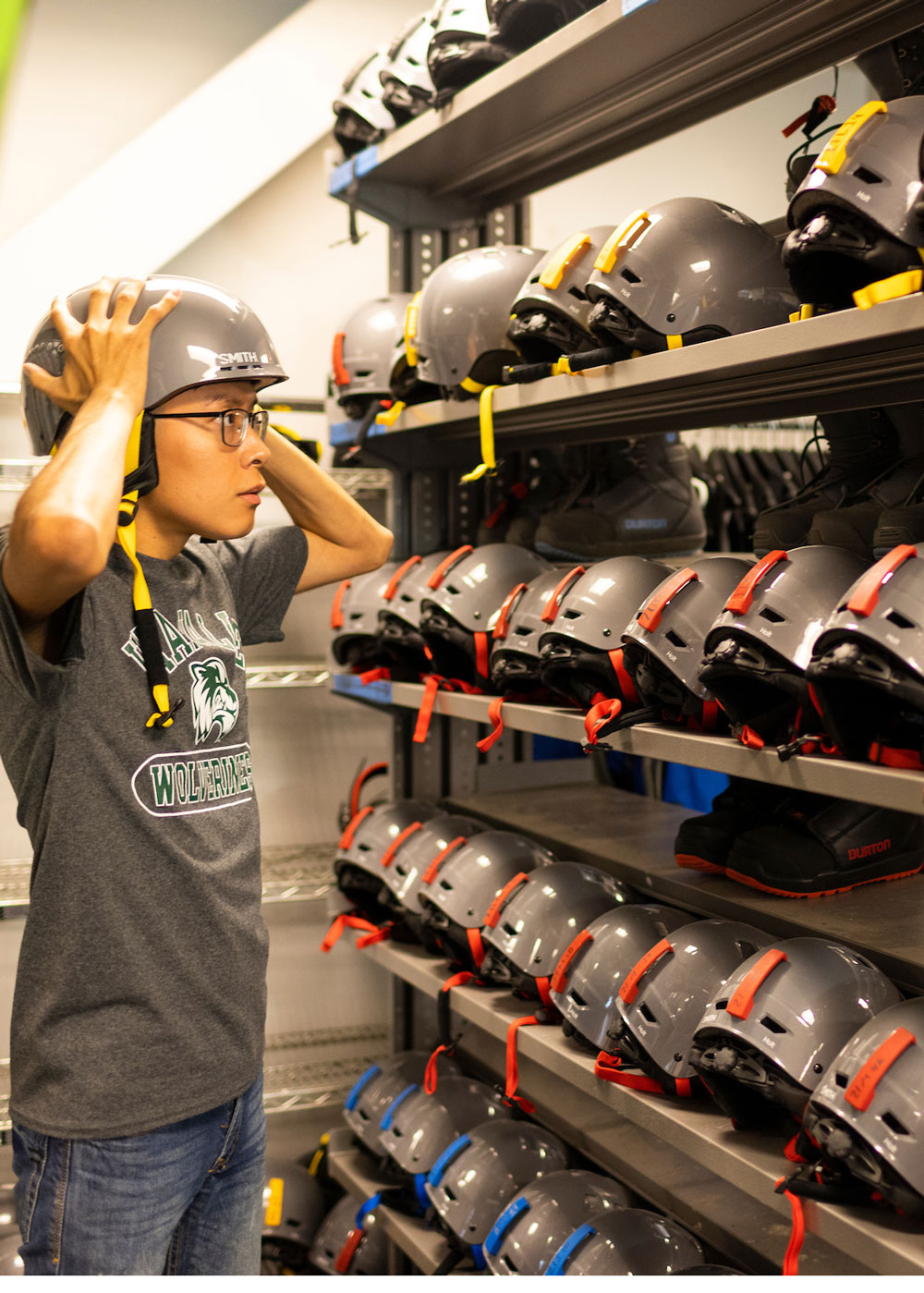A person trying snowboard helmet next to large stock of helmets