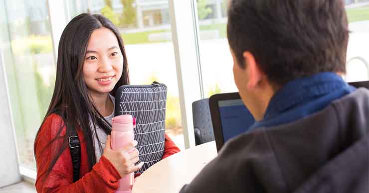 Female student talking with a male employee.  Female student is asian and is smiling about the covnerstaion.
