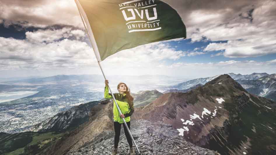 Female stading on the top of a mountain waving a UVU flag