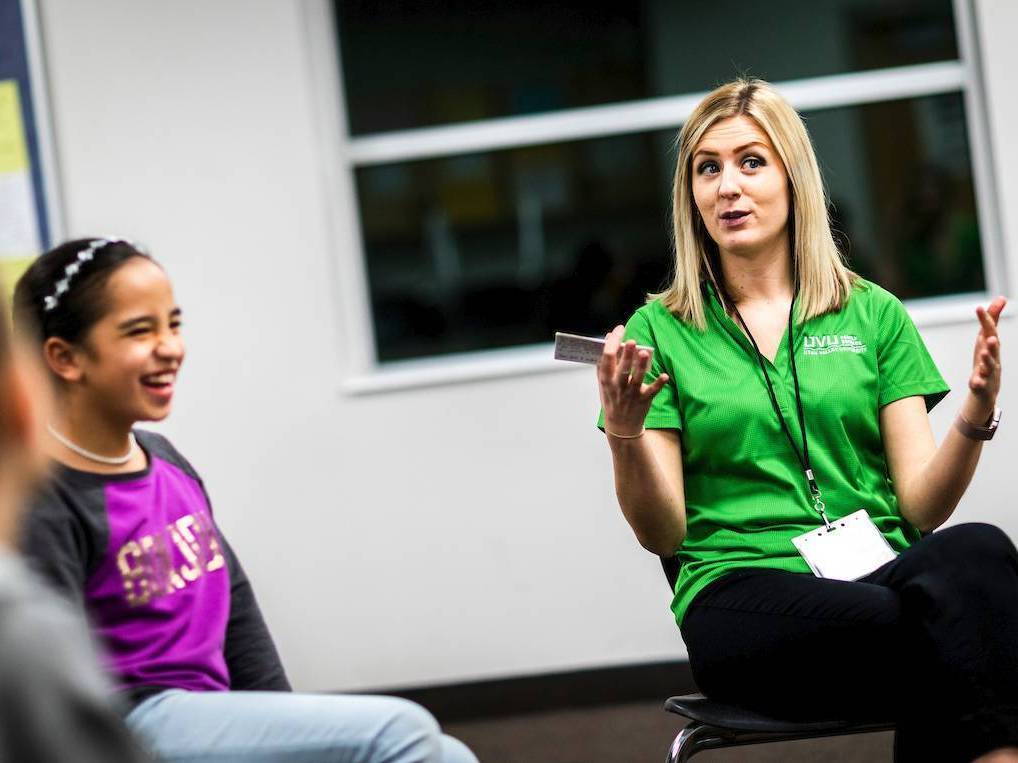 An intern in a green shirt speaks to children while one laughs