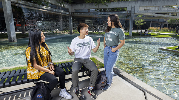 Three students around a bench next to a water feature in the UVU courtyard.