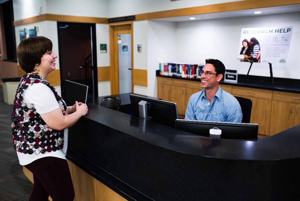 A librarian helping a student while seated at the library’s Research Help Desk.