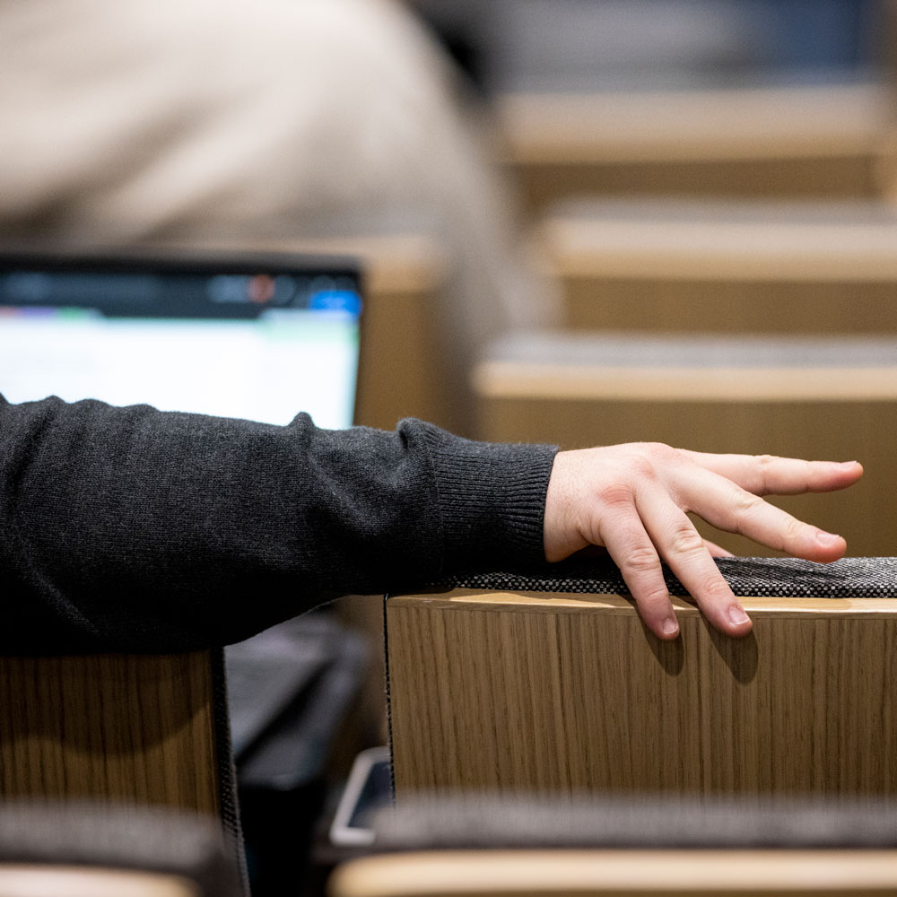 Hand on back of classroom chair, blurry laptop and more chairs in background