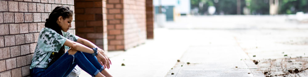 Woman sitting on curb against wall looking sad