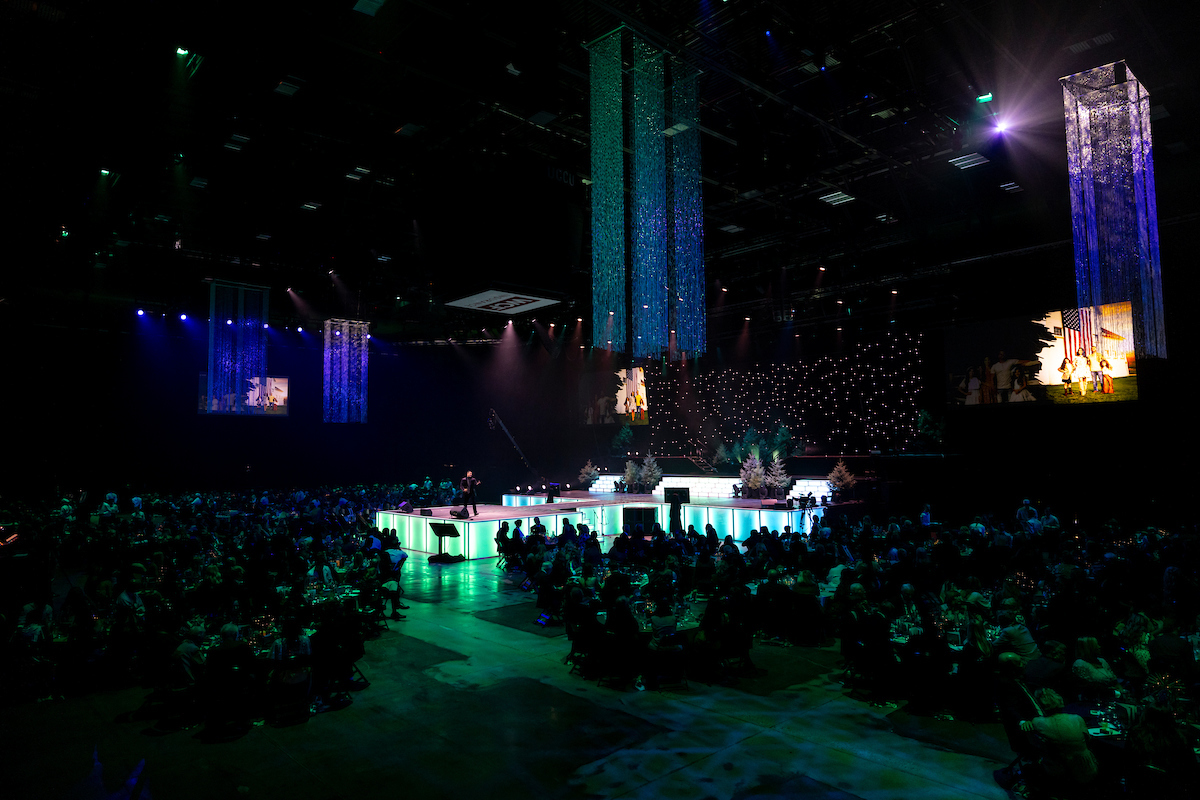 large arena with stage and lighting surrouned by tables of guests