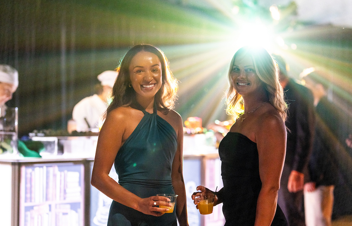 two women in gowns pose with drinks at event