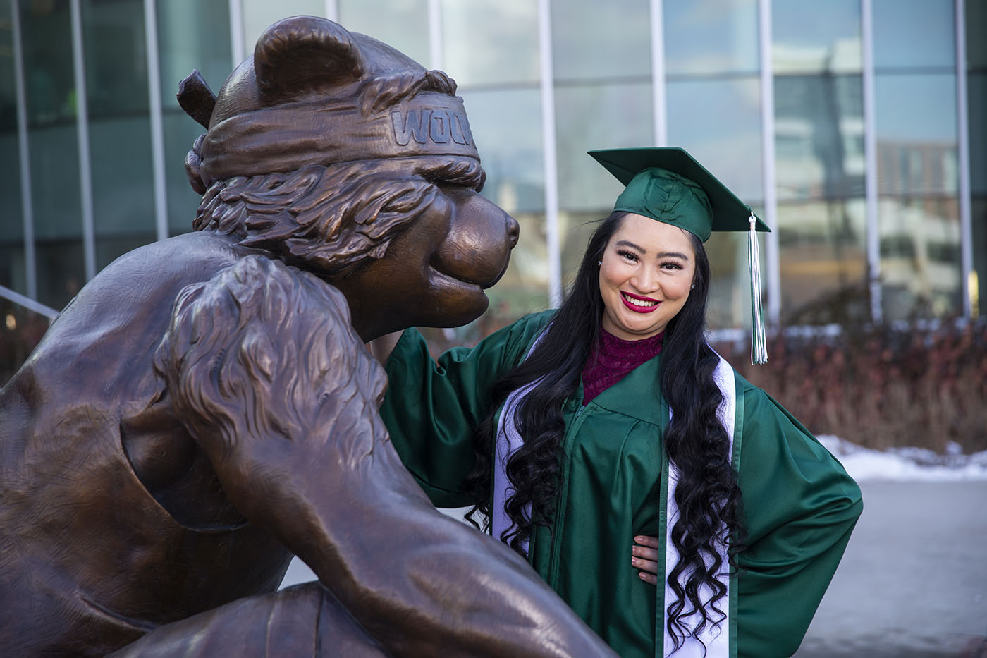 graduate poses with statue of Willy the Wolverine