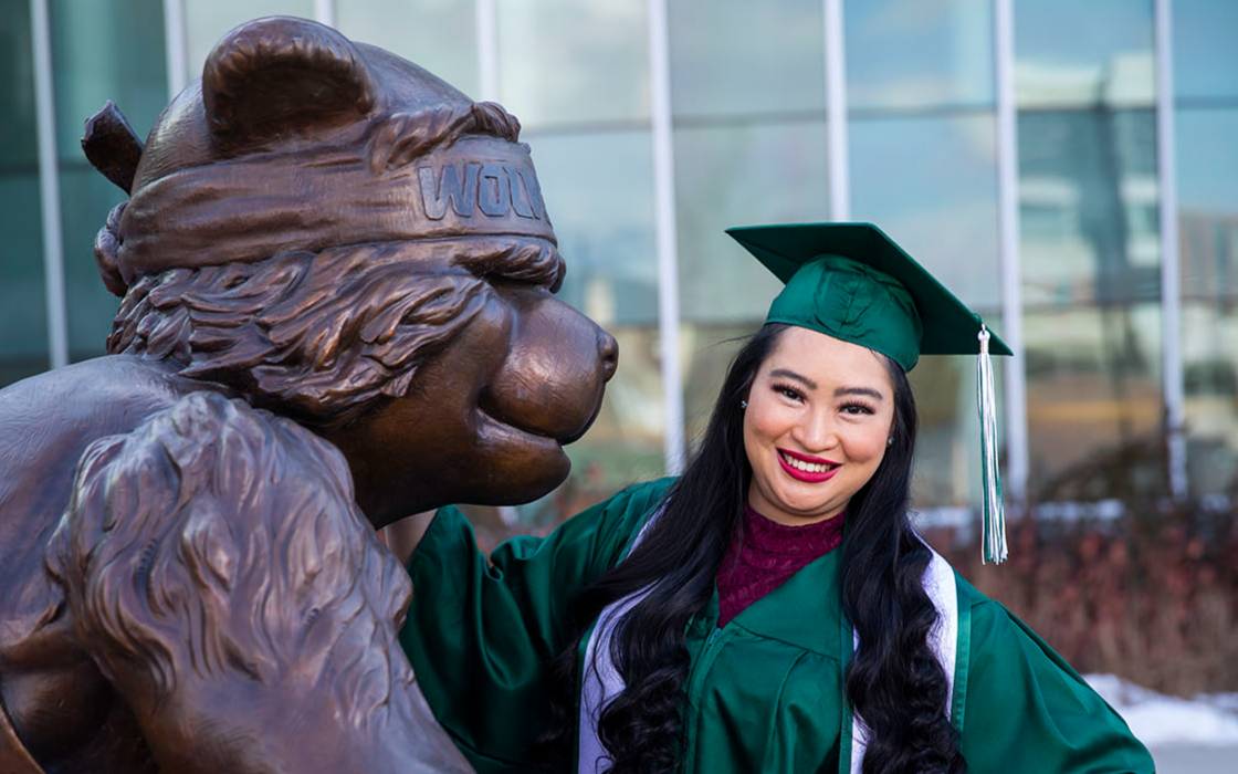 graduate poses with statue of Willy the Wolverine