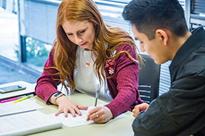 A girl and boy write on a paper while sitting at a desk