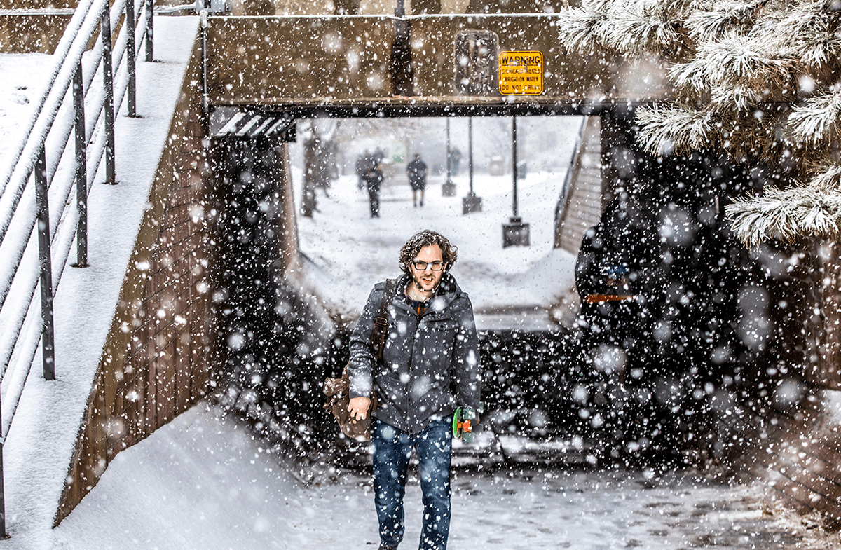 A man walks towards the camera under a bridge in the snow