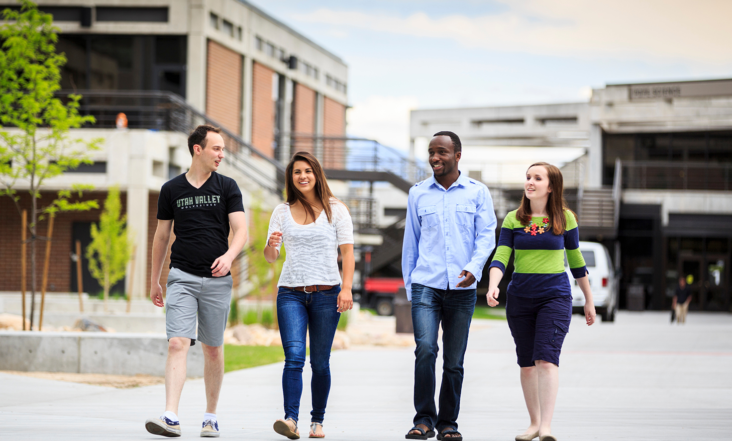 Four students smiling and walking towards the camera on UVU campus
