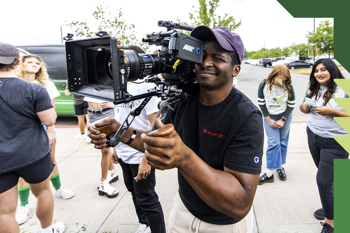 A UVU student wearing a black t-shirt and a purple cap operates a video camera. A UVU student wearing a black t-shirt and a purple cap operates a video camera.