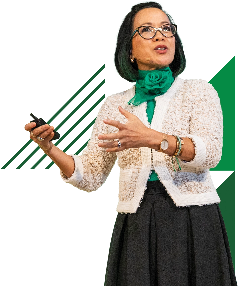Wearing a white top, black skirt, and glasses, President Tuminez speaks at an event. 