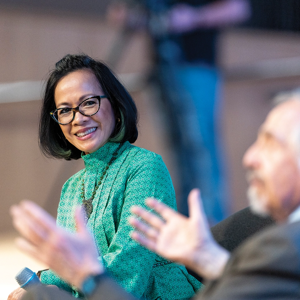Wearing a green dress, President Tuminez smiles as she speaks with Dr. Arthur Kleinman at the fall 2024 presidential lecture. 