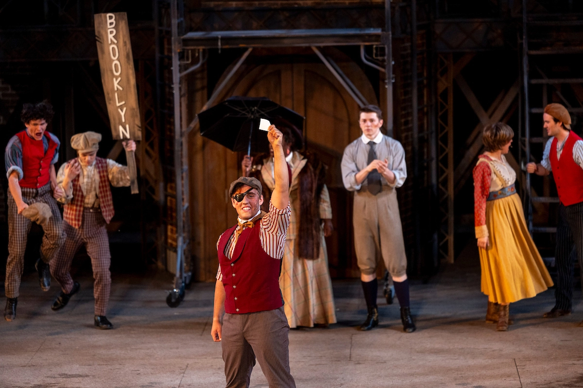 Photograph of Newsies actors on stage mid-scene. Photograph of Newsies actors on stage mid-scene.