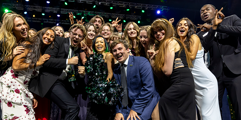 Former UVU President Astrid S. Tuminez smiles on stage at the UVU President’s Scholarship Ball with former Student Body President Kyle Cullimore and students from UVU’s Presidential 100 program. 