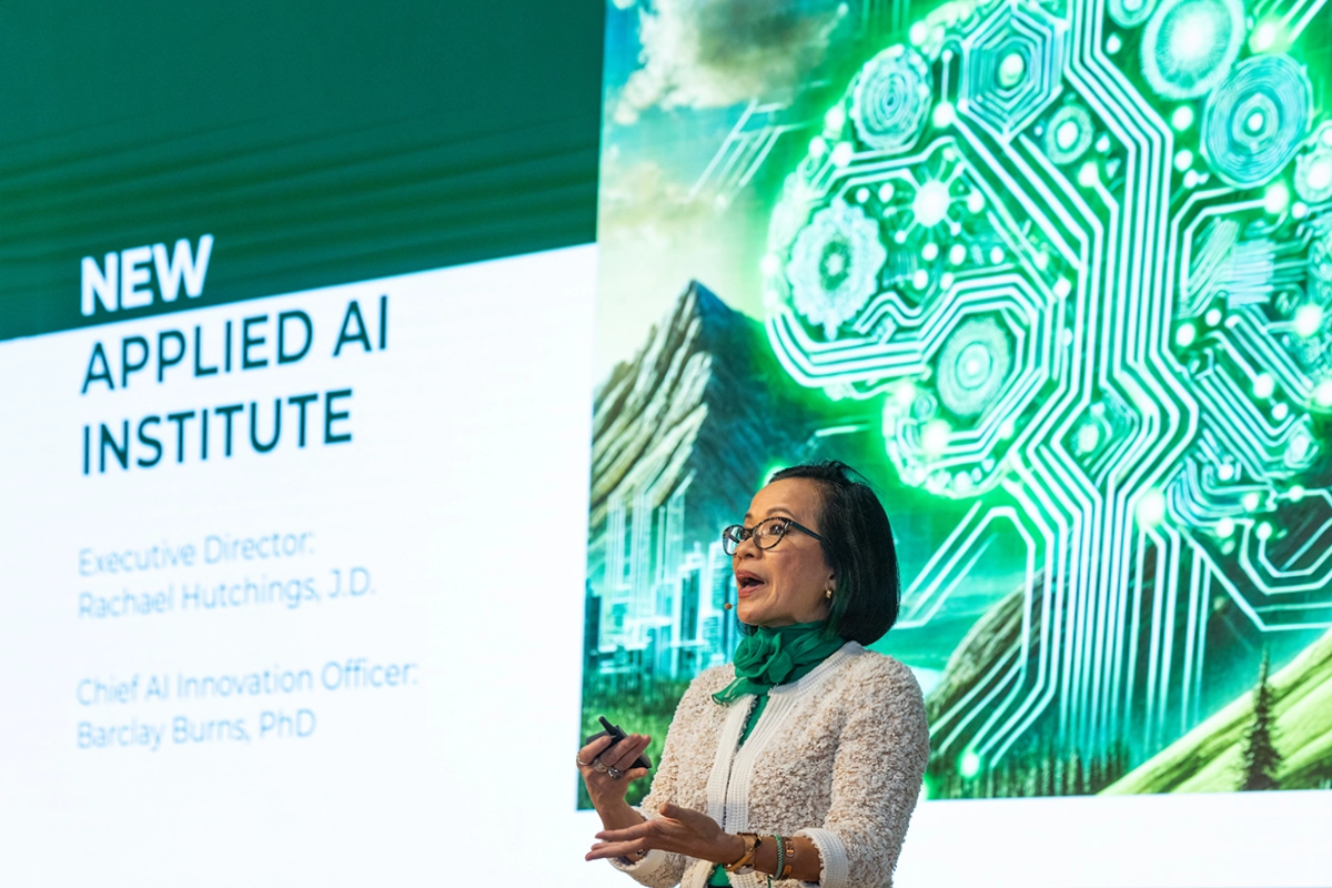 Astrid Tuminez speaks in front of a presentation screen that reads, 'New Applied AI Institute'. Astrid Tuminez speaks in front of a presentation screen that reads, 'New Applied AI Institute'.