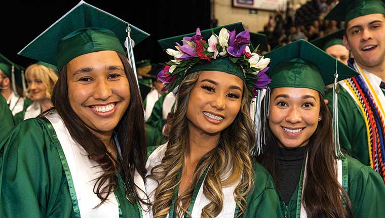 A group of graduates wearing green UVU regalia smile during UVU’s 2023 commencement ceremony. 