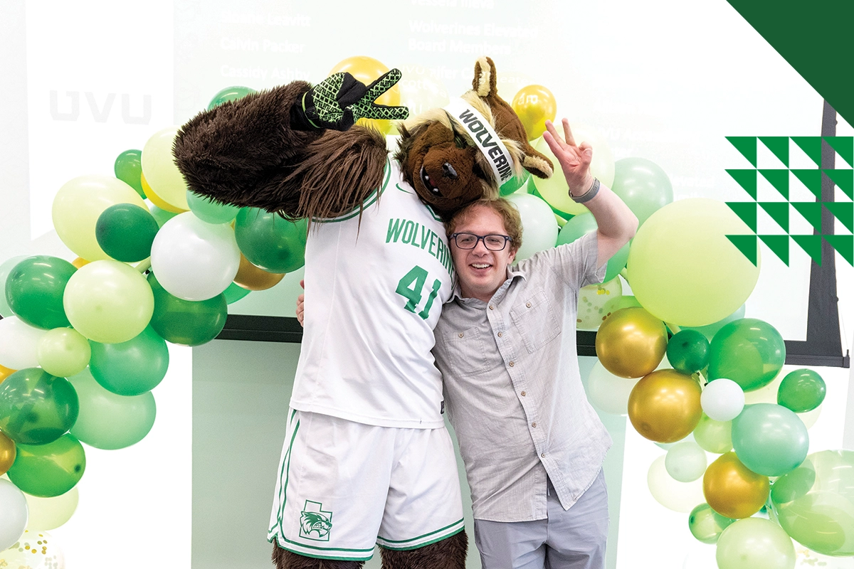 Willy the Wolverine and a student in a gray button-down shirt pose together, making “peace signs” with their hands. Willy the Wolverine and a student in a gray button-down shirt pose together, making “peace signs” with their hands.
