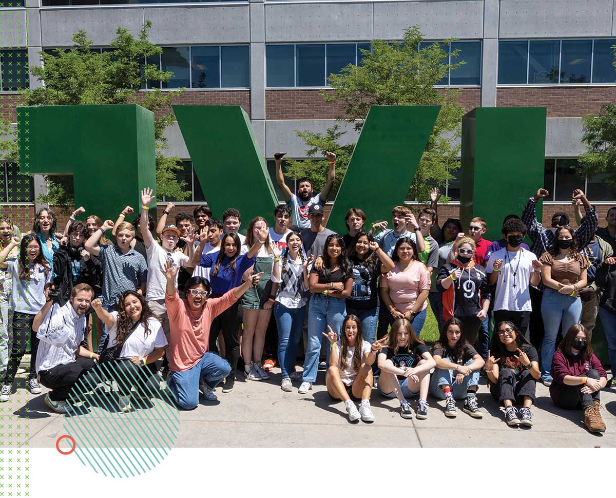 A large group of Latinos of Tomorrow Summer Bridge Program participants tour UVU’s Orem Campus, posing near large, green UVU letters. 
