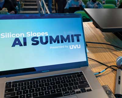 Photo of a laptop with a presentation on the screen that reads: Silicon Slopes AI Summit presented by UVU. 