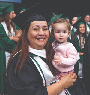 A UVU graduate, wearing UVU regalia, smiles while holding her young daughter at UVU’s 2023 commencement ceremony. 
