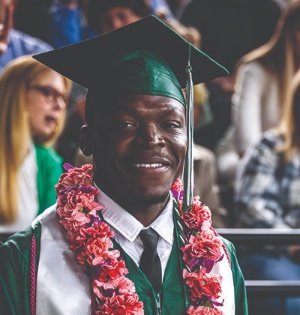 A student wearing a pink floral lei and green UVU regalia smiles during UVU’s 2023 commencement ceremony. 