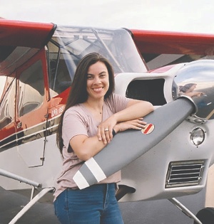 UVU aviation student Nicole Robbins smiles while posing next to a small airplane. 