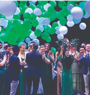 Group celebrates amid falling green and white balloons.