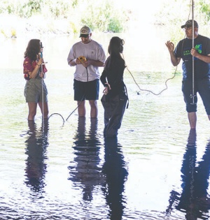 Two UVU professors and two UVU students stand in shallow water at Utah Lake, using instruments to measure water flow. 