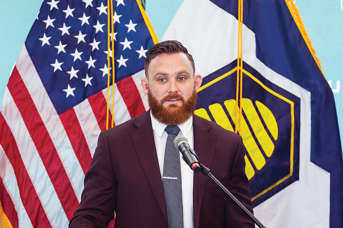 Standing in front of the American flag and the Utah flag, Brandon Amacher speaks at a podium emblazoned with the UVU logo. Standing in front of the American flag and the Utah flag, Brandon Amacher speaks at a podium emblazoned with the UVU logo.