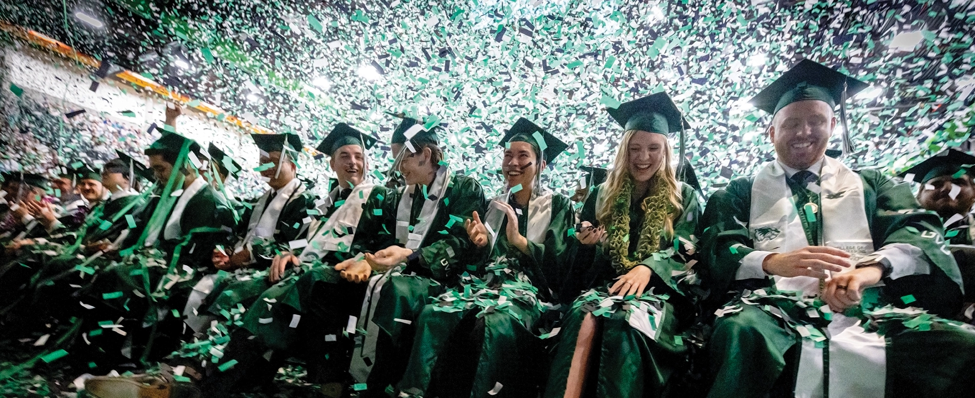 A wide shot of graduates having a great time as confetti falls from the ceiling. A wide shot of graduates having a great time as confetti falls from the ceiling.