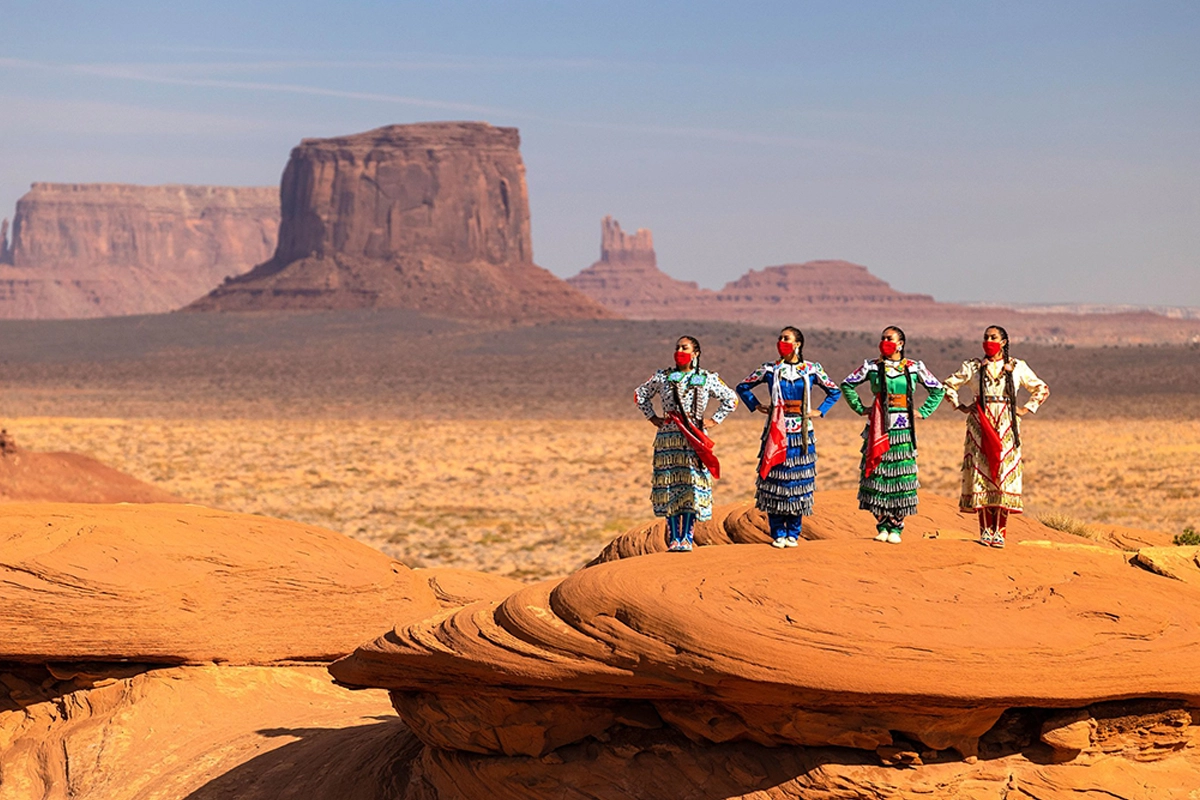 Photo of 4 Navajo women in full traditional dress stand on scenic red rock. Photo of 4 Navajo women in full traditional dress stand on scenic red rock.