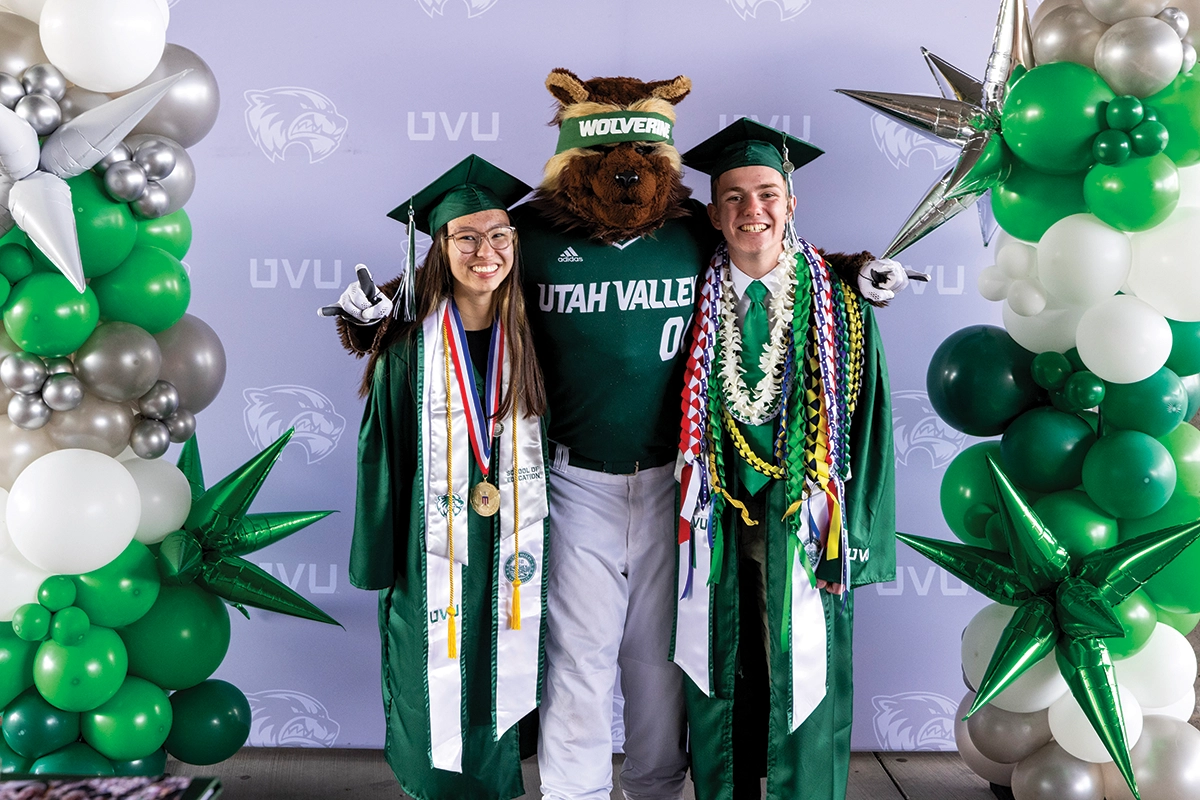Two graduates pose with Willy near an ornate baloon arch. Two graduates pose with Willy near an ornate baloon arch.