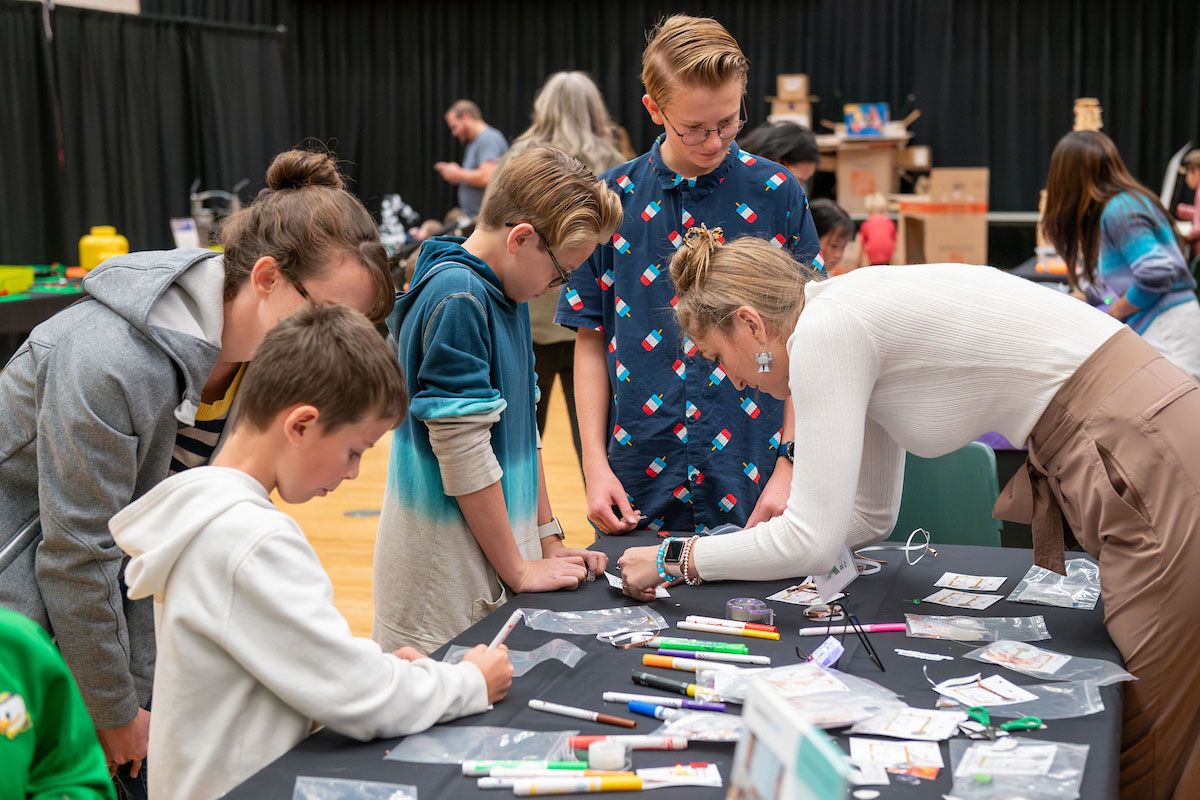 A hands-on MakerCon table with an instructor helping kids with a project. A hands-on MakerCon table with an instructor helping kids with a project.