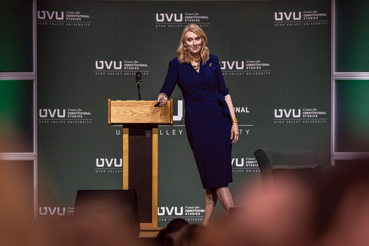 Wearing a dark blue dress, Sharon McMahon stands at a lectern in front of a UVU Center for Constitutional Studies backdrop. Wearing a dark blue dress, Sharon McMahon stands at a lectern in front of a UVU Center for Constitutional Studies backdrop.