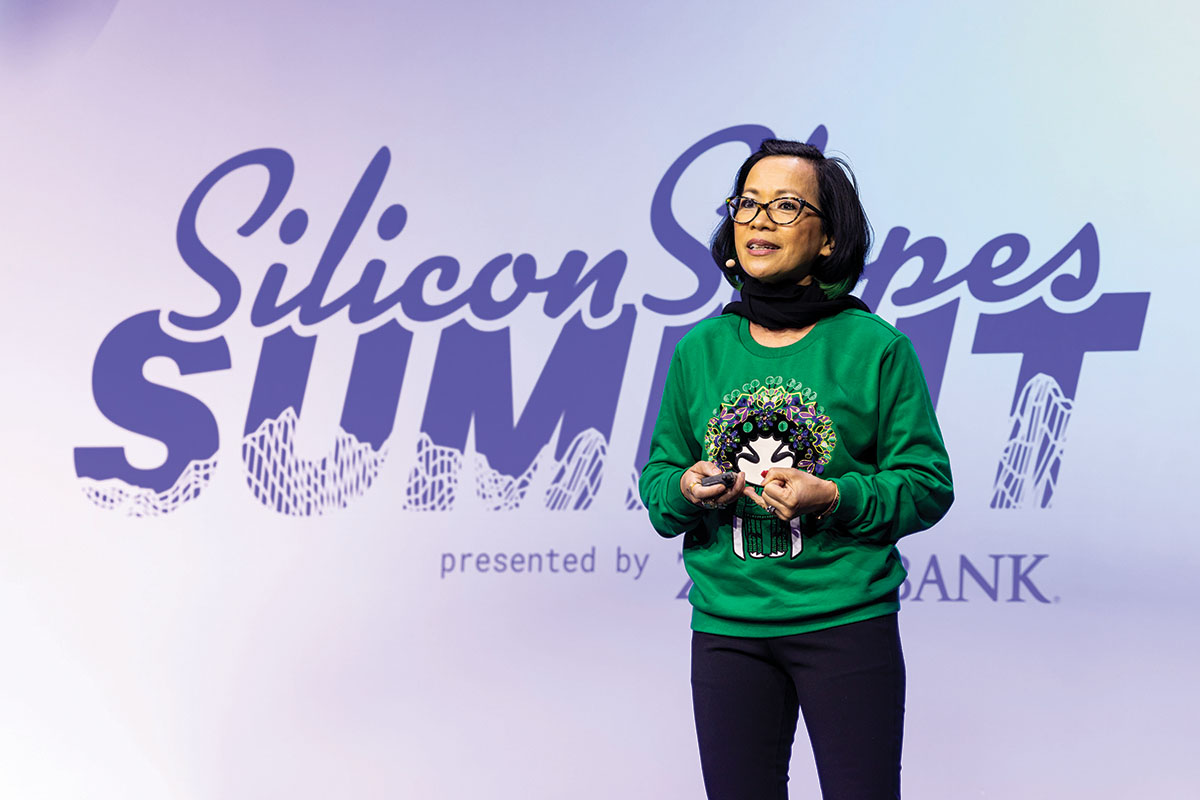 Wearing a green sweater, President Tuminez speaks on stage at the 2025 Silicon Slopes Summit in the UCCU Center on UVU’s Orem Campus. 