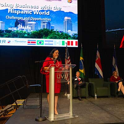 Woman in a red dress speaks at a podium at 'Doing Buisness with the Hispanic World' presentation. Woman in a red dress speaks at a podium at 'Doing Buisness with the Hispanic World' presentation.