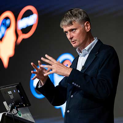 Neil Lawrence gives a talk on AI at a podium. Neil Lawrence gives a talk on AI at a podium.