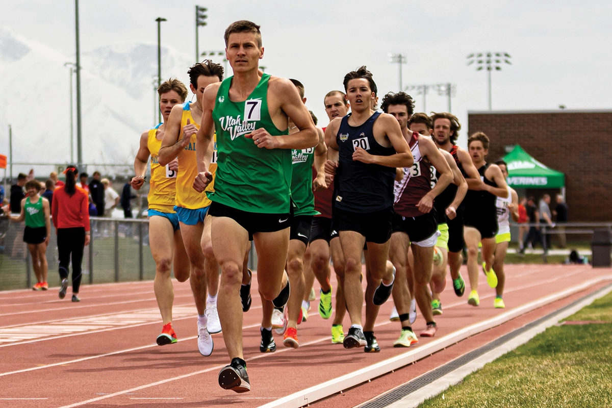 Track and field team members run on an outdoor track, with a UVU track and field team member in a green Utah Valley jersey at the front of the group. Track and field team members run on an outdoor track, with a UVU track and field team member in a green Utah Valley jersey at the front of the group.