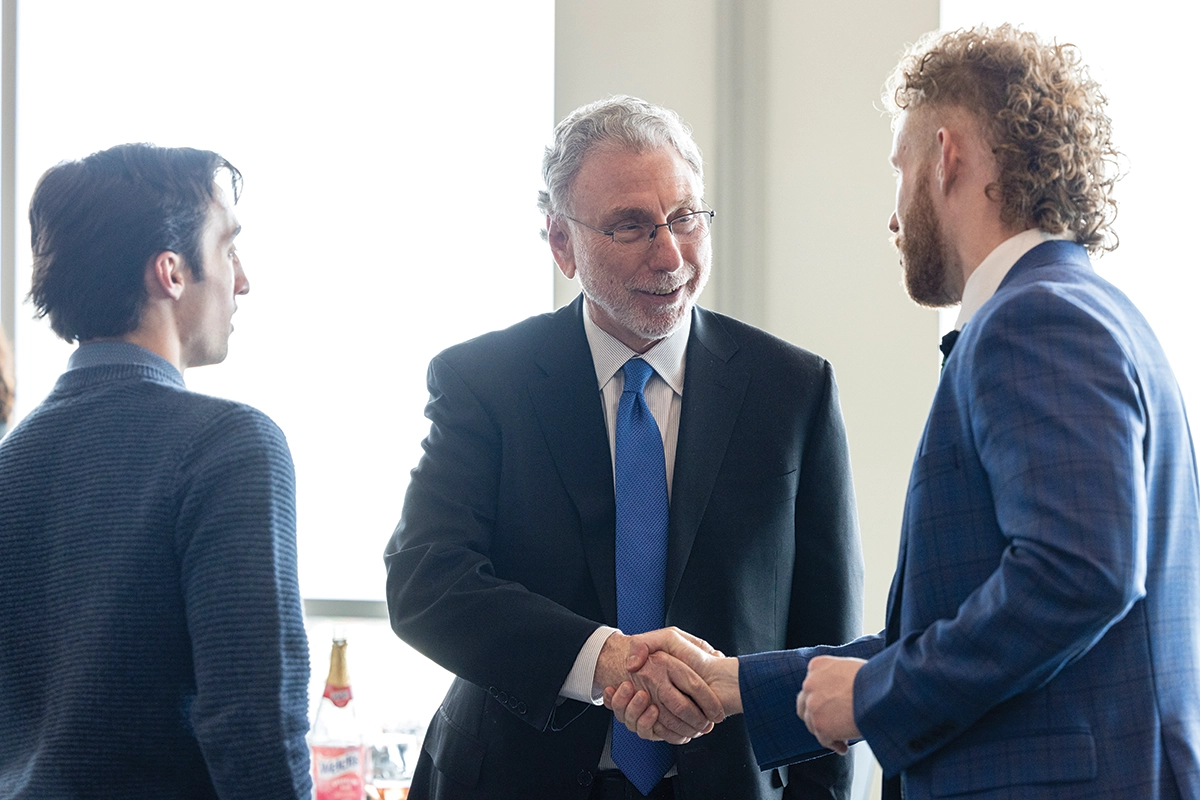 Wearing a suit and tie, Pulitzer Prize-winning journalist Martin Baron shakes hands with a UVU student while another student looks on. 