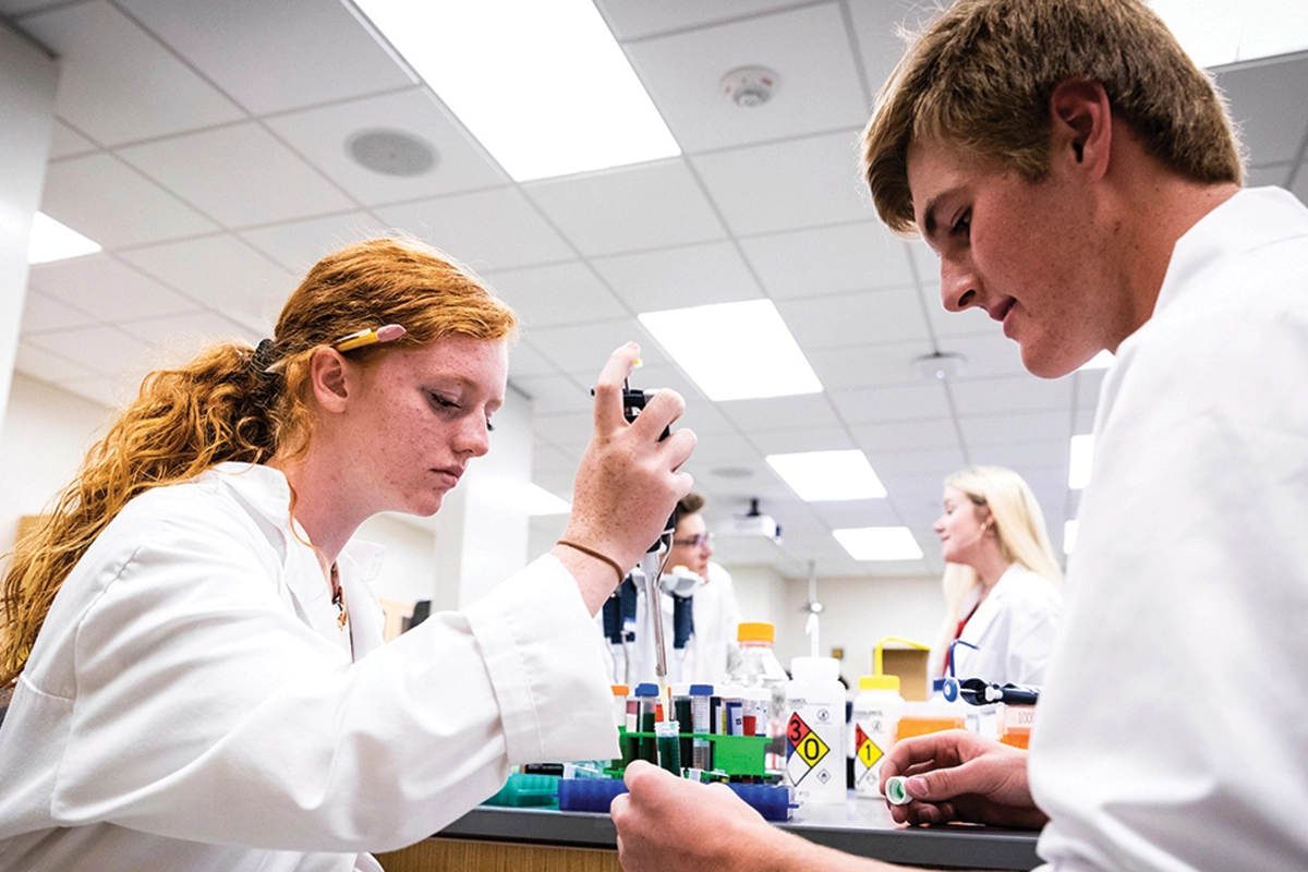 UVU students wearing white lab coats conduct work in a lab. 