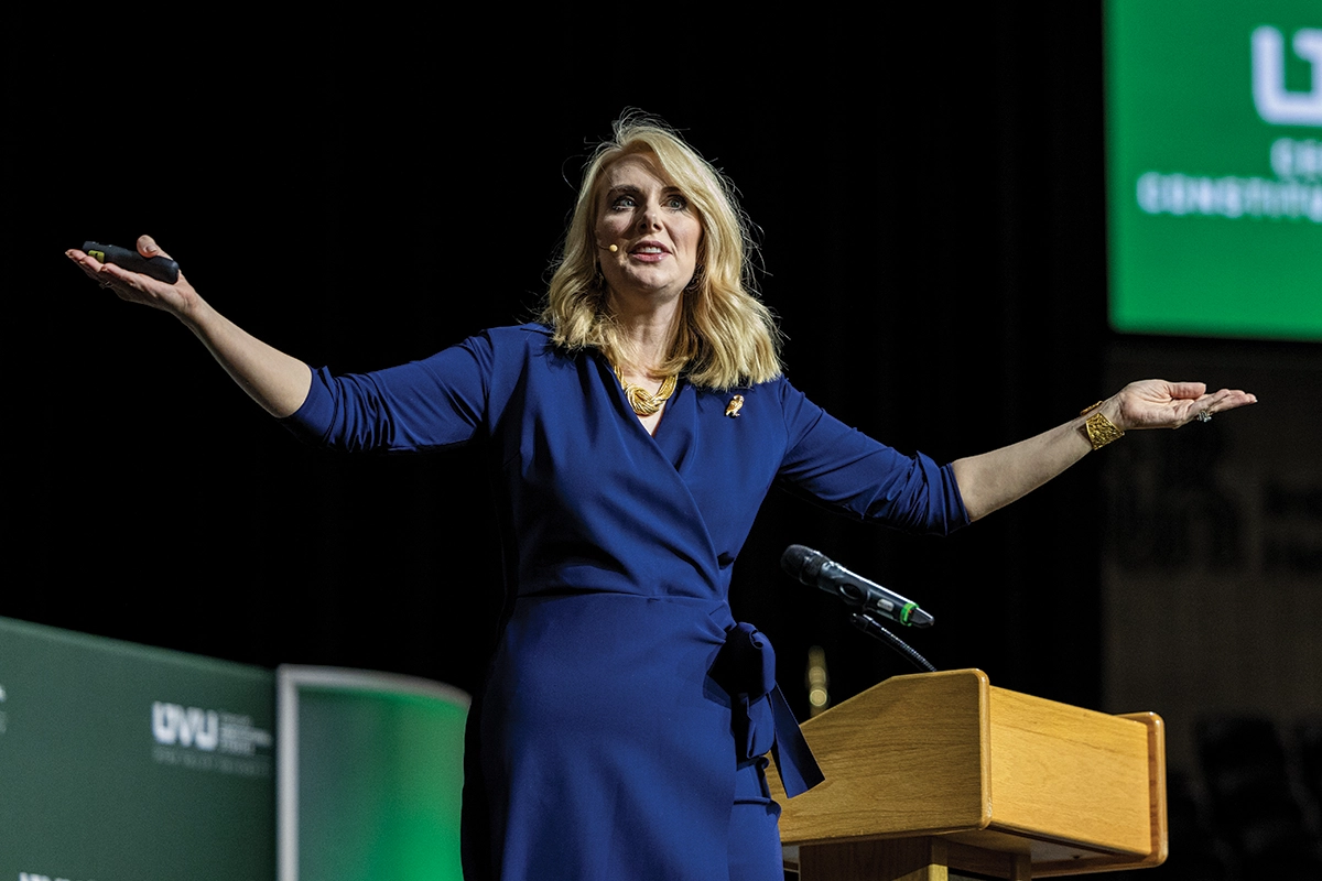 Sharon McMahon, wearing a blue dress, speaks on stage during an event at the UCCU Center.