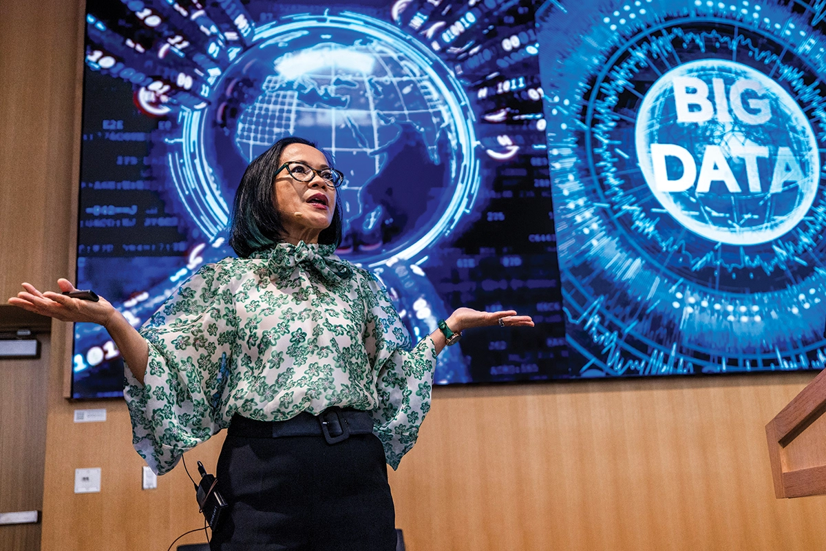 President Tuminez, wearing a green and white floral blouse and black pants, speaks on stage during the UVU Data Summit event. 