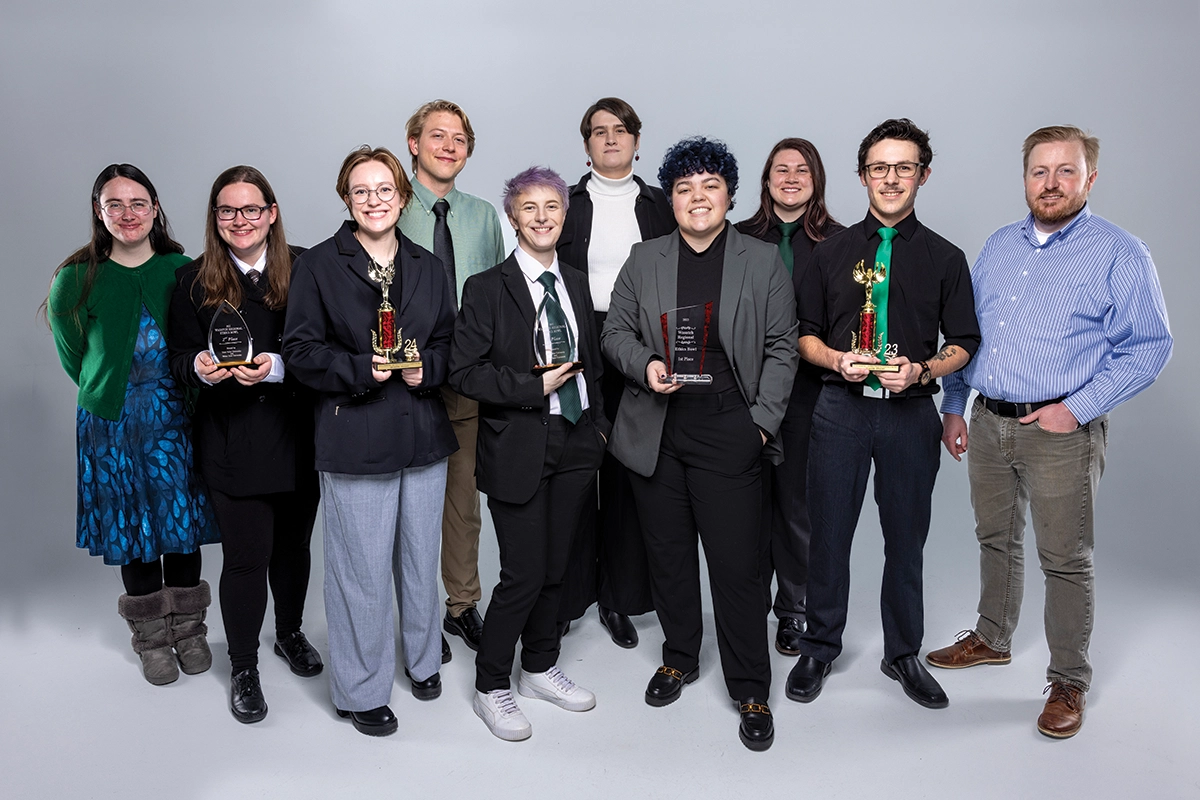 UVU Ethics Bowl team members pose for a photo, some holding trophies the team has won. 