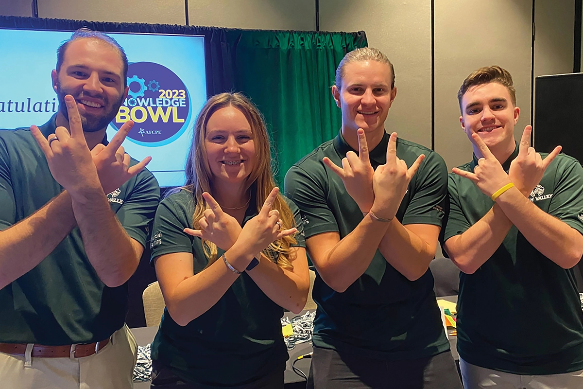 Four students from the UVU financial planning team do the Wolverine sign with their hands at the AFCPE 2023 Knowledge Bowl. 