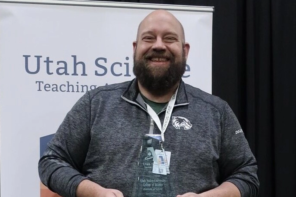 A representative from the Utah College of Science smiles while wearing a jacket emblazoned with the UVU Wolverine logo.