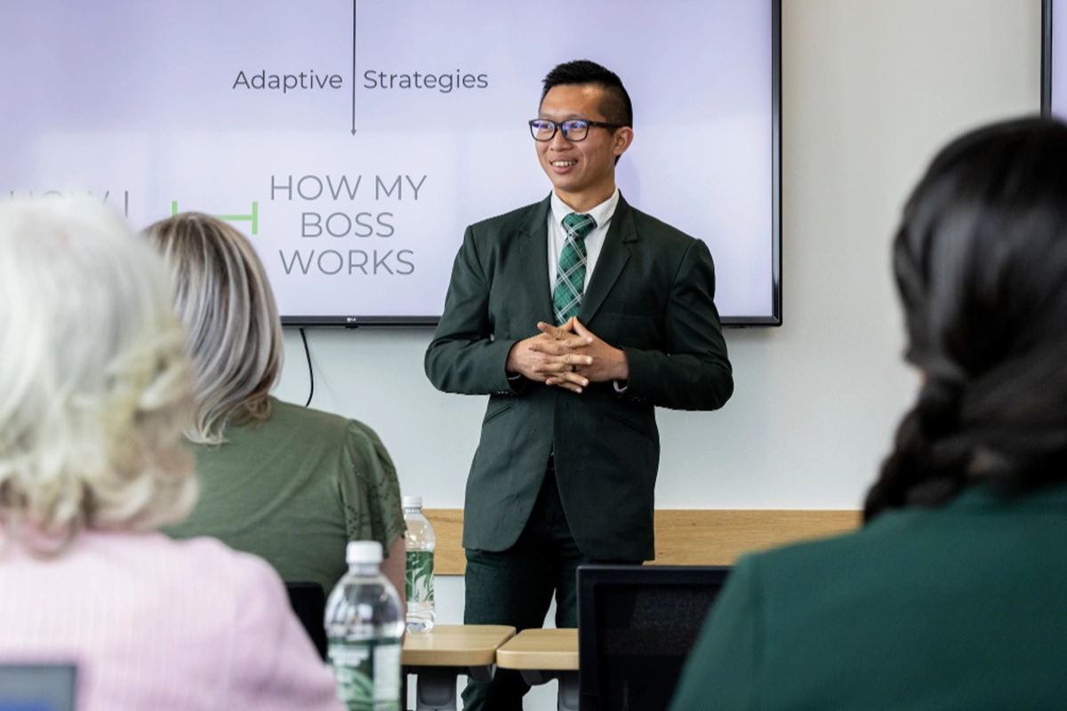 A student in a suit and green tie speaks in front of an audience. 