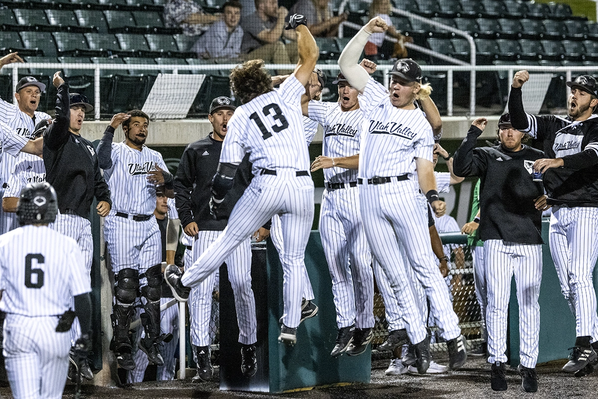 UVU baseball team members, wearing Utah Valley jerseys, cheer and celebrate on a baseball field. 