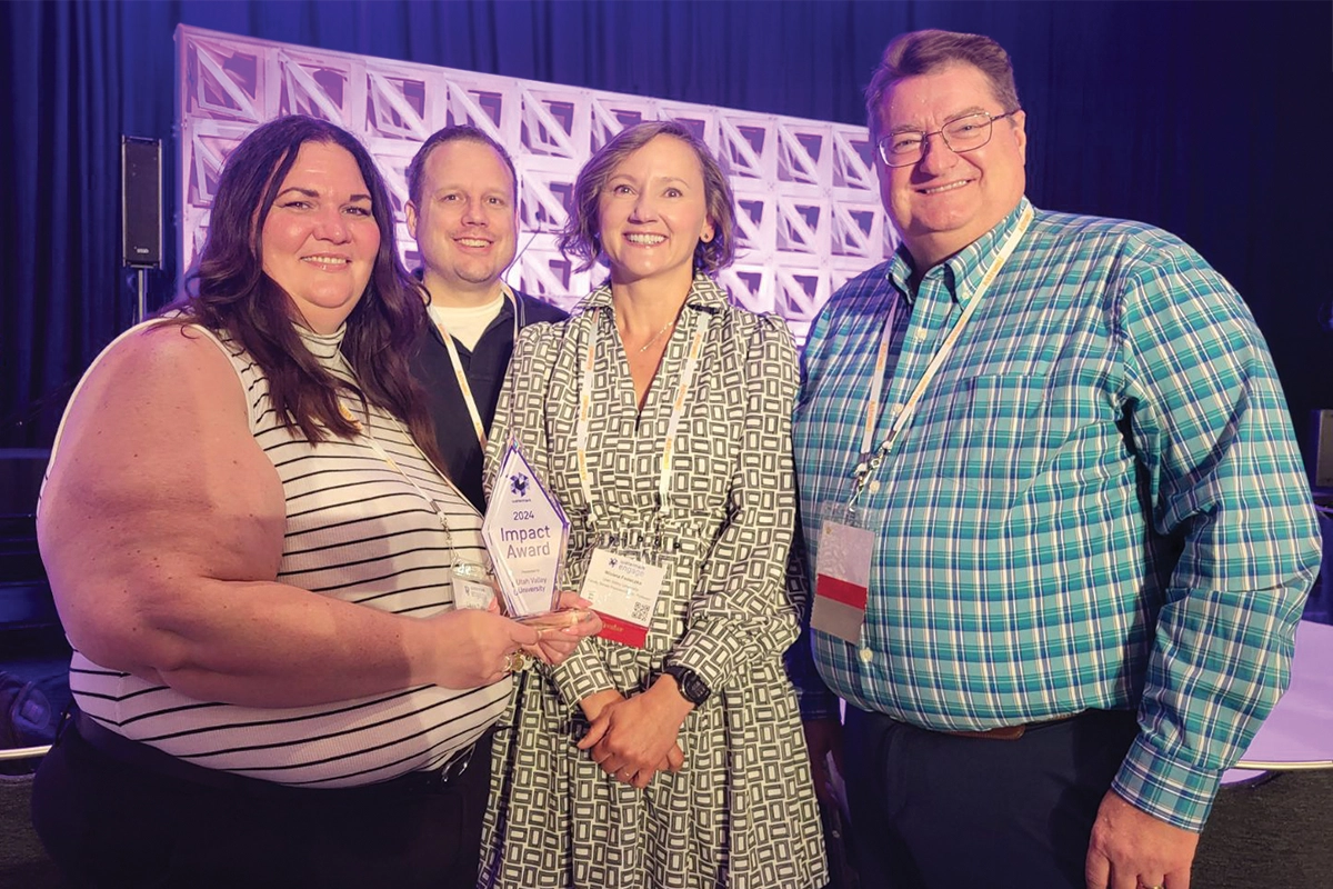 UVU’s Faculty Success team — Laurie Toro, Trevor Morris, Bryan Cowley, and Wioleta Fedeczko, smile together at an award ceremony with the Impact Award trophy they won. 